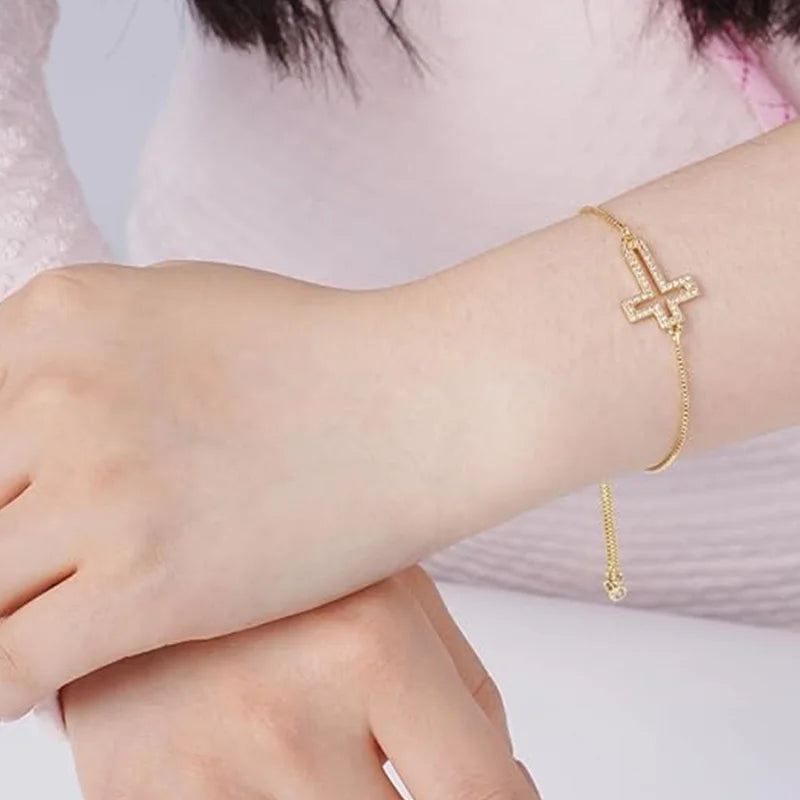 A close-up of a hand wearing an adjustable gold plated cross bracelet with cubic zirconia stones.