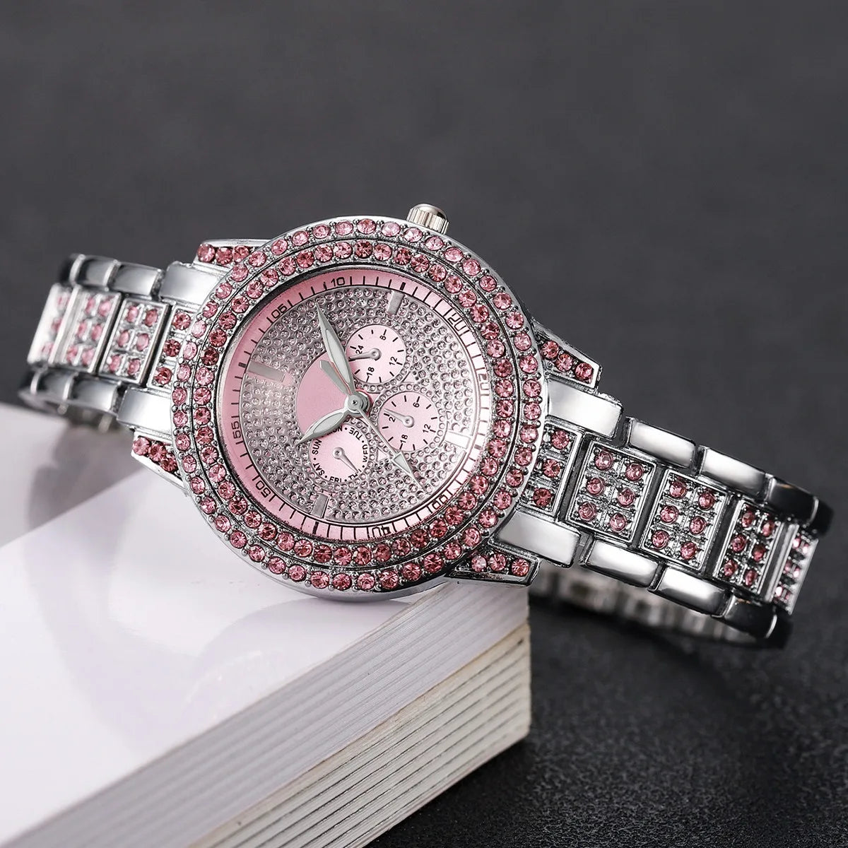 A silver watch with a pink diamond rhinestone bezel and bracelet resting on a white surface.