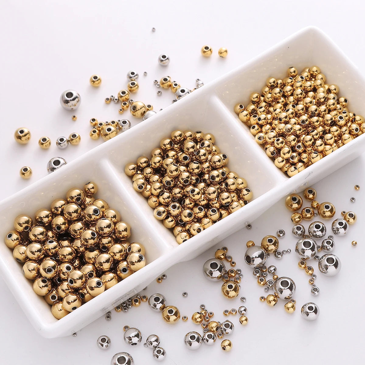 A collection of gold and silver spacer beads scattered on a white surface.