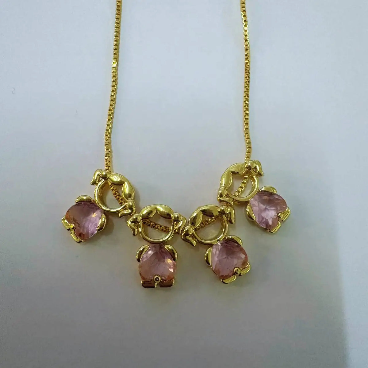 Goldener Anhänger mit rosa Edelsteinen auf goldener Kette.