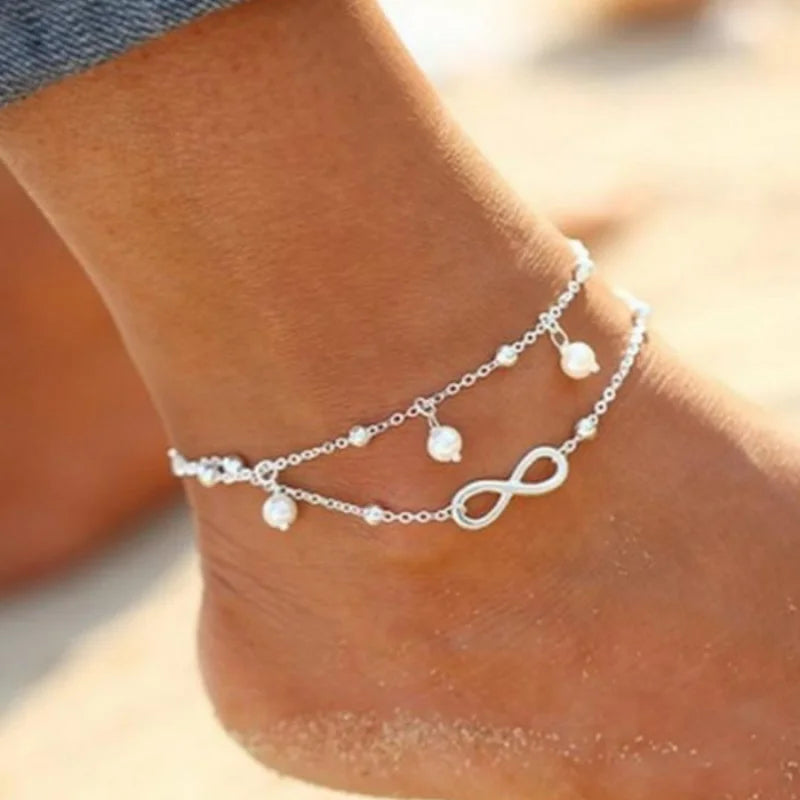 A close-up of a boho silver-plated friendship anklet with small pearl charms worn on a person's ankle.