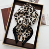 A black and tan leopard print silk scarf tied in a bow displayed in a wooden frame.