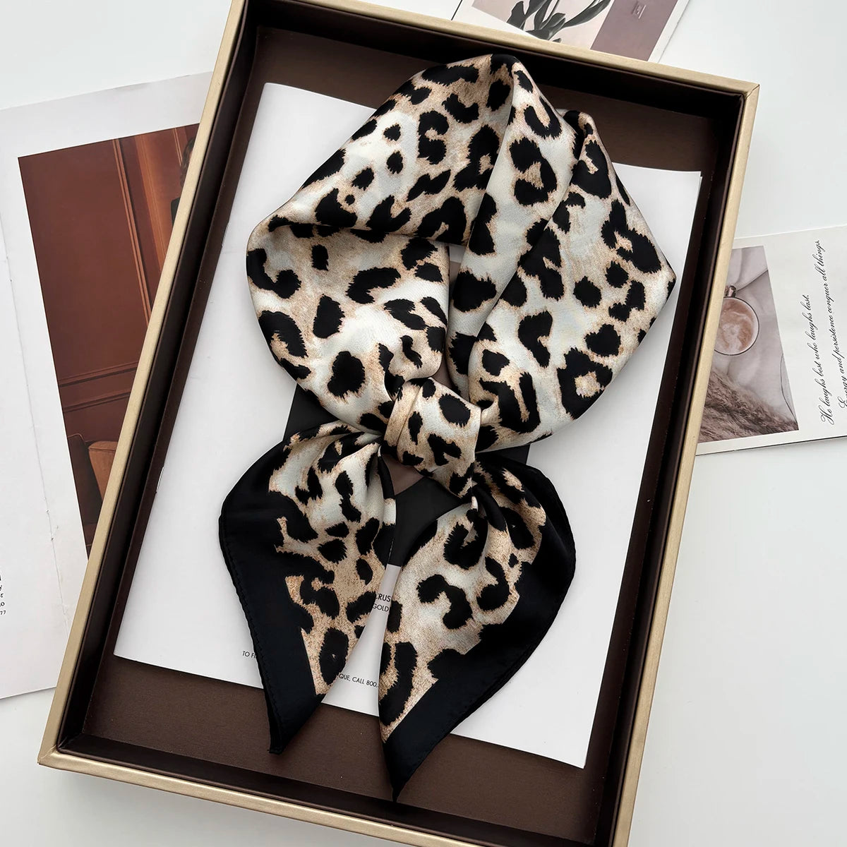 A black and tan leopard print silk scarf tied in a bow displayed in a wooden frame.