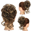 A close-up of a woman's hair styled in a voluminous, messy bun with loose curls and highlights.