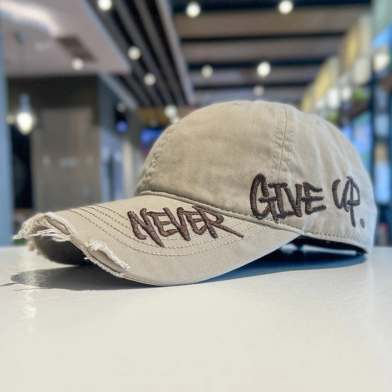 A light beige vintage washed cotton baseball cap with embroidered text that reads NEVER GIVE UP.