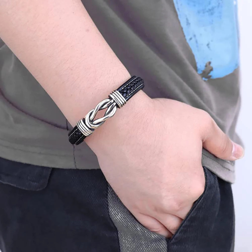 A close-up of a black leather knot bracelet with silver accents worn on a wrist.