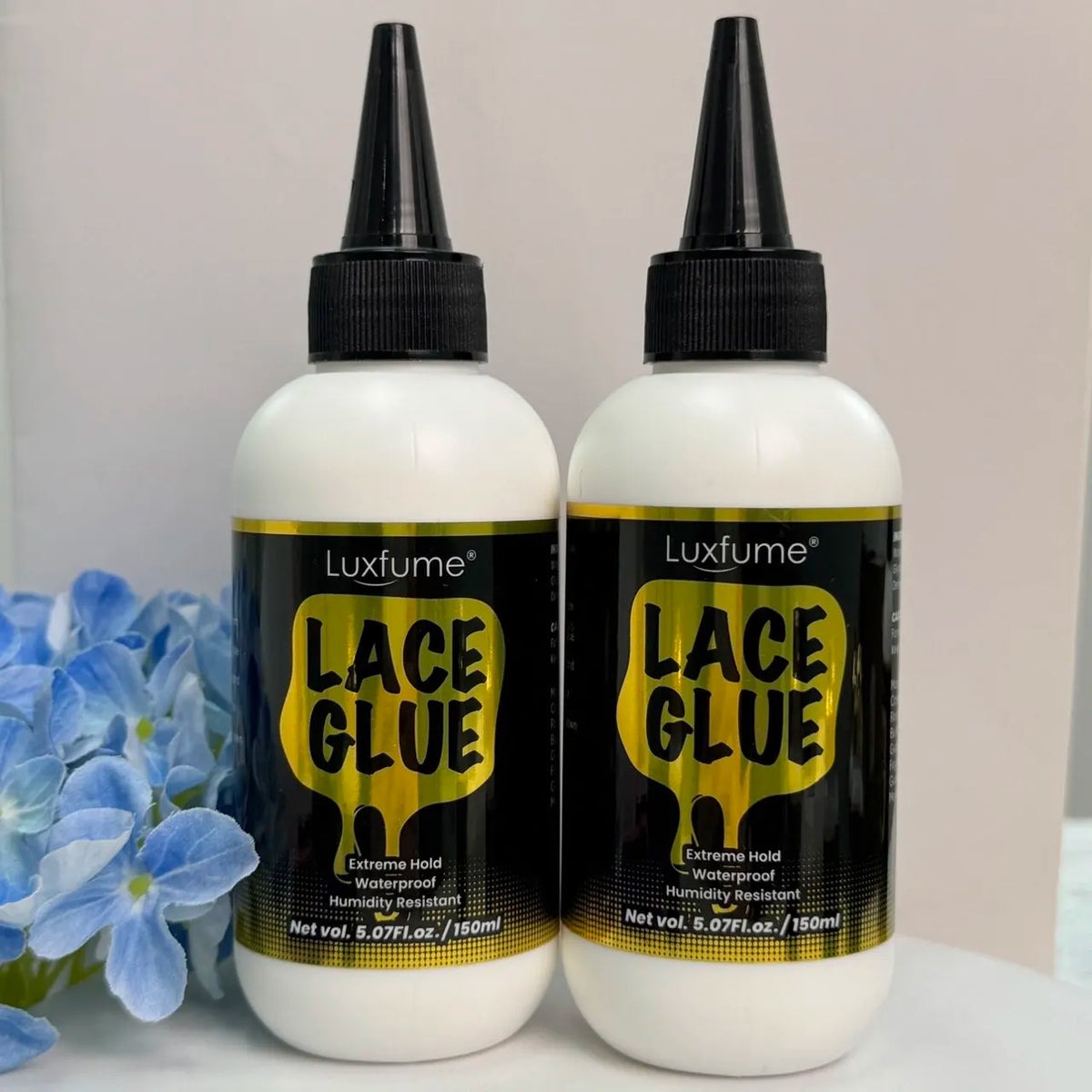 Zwei Flaschen Luxfume Lace Glue mit schwarzen Pipettenkappen und weißen Körpern