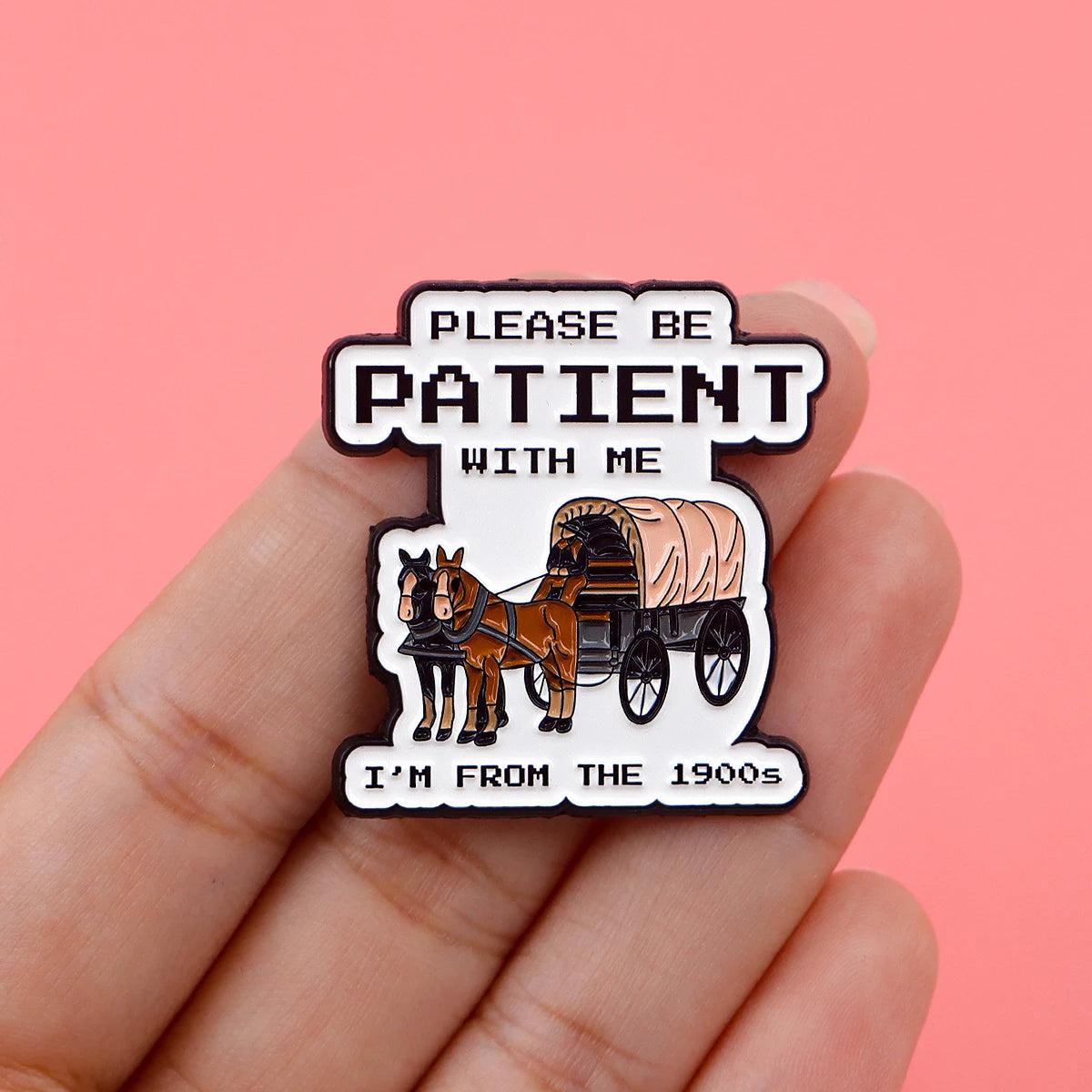 A black enamel pin featuring text that reads Please be patient with me and an illustration of a horse-drawn wagon from the 19