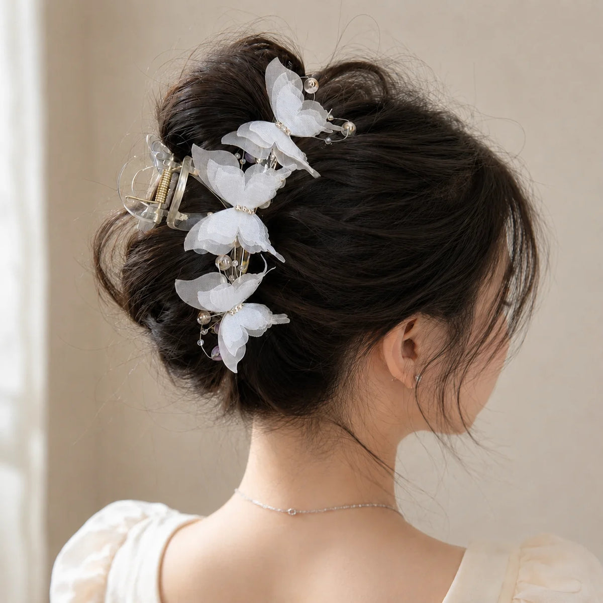 A close-up of a woman's dark hair styled in an elegant updo adorned with pearl rhinestone butterfly hair claw clips.