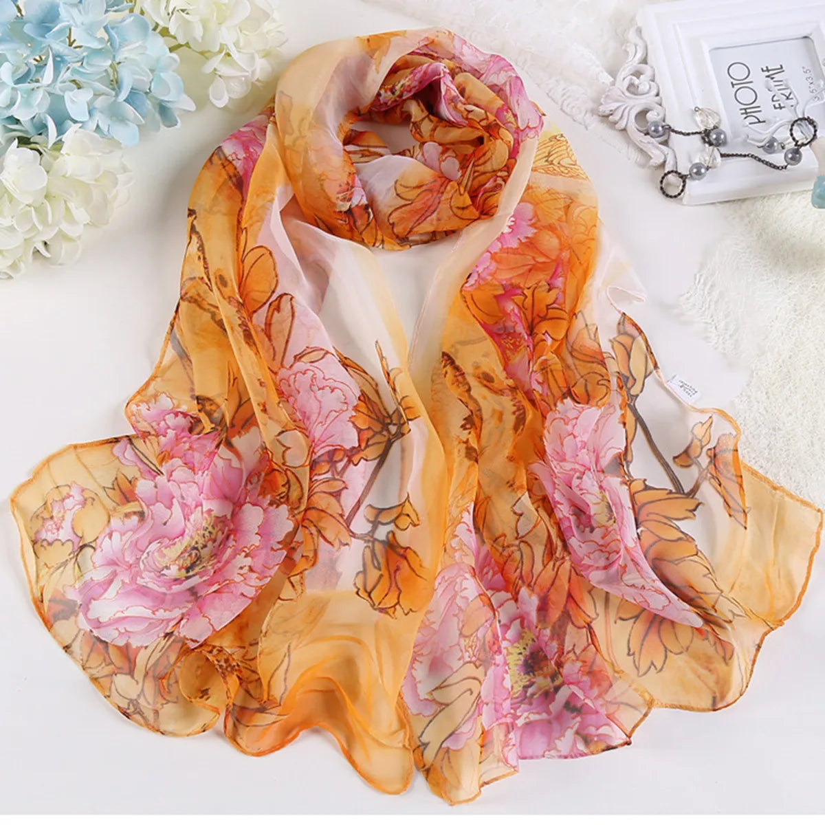 Un châle en soie floral élégant aux tons orange et rose avec des motifs de feuilles.