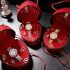 A red velvet jewelry box with a lid open, displaying various rhinestone heart-shaped necklaces and bracelets.