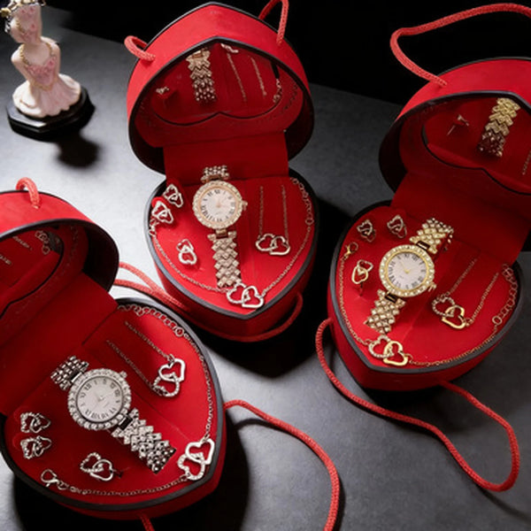 A red velvet jewelry box with a lid open, displaying various rhinestone heart-shaped necklaces and bracelets.