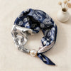 A navy blue silk scarf with white and beige floral patterns tied with a pearl knot.