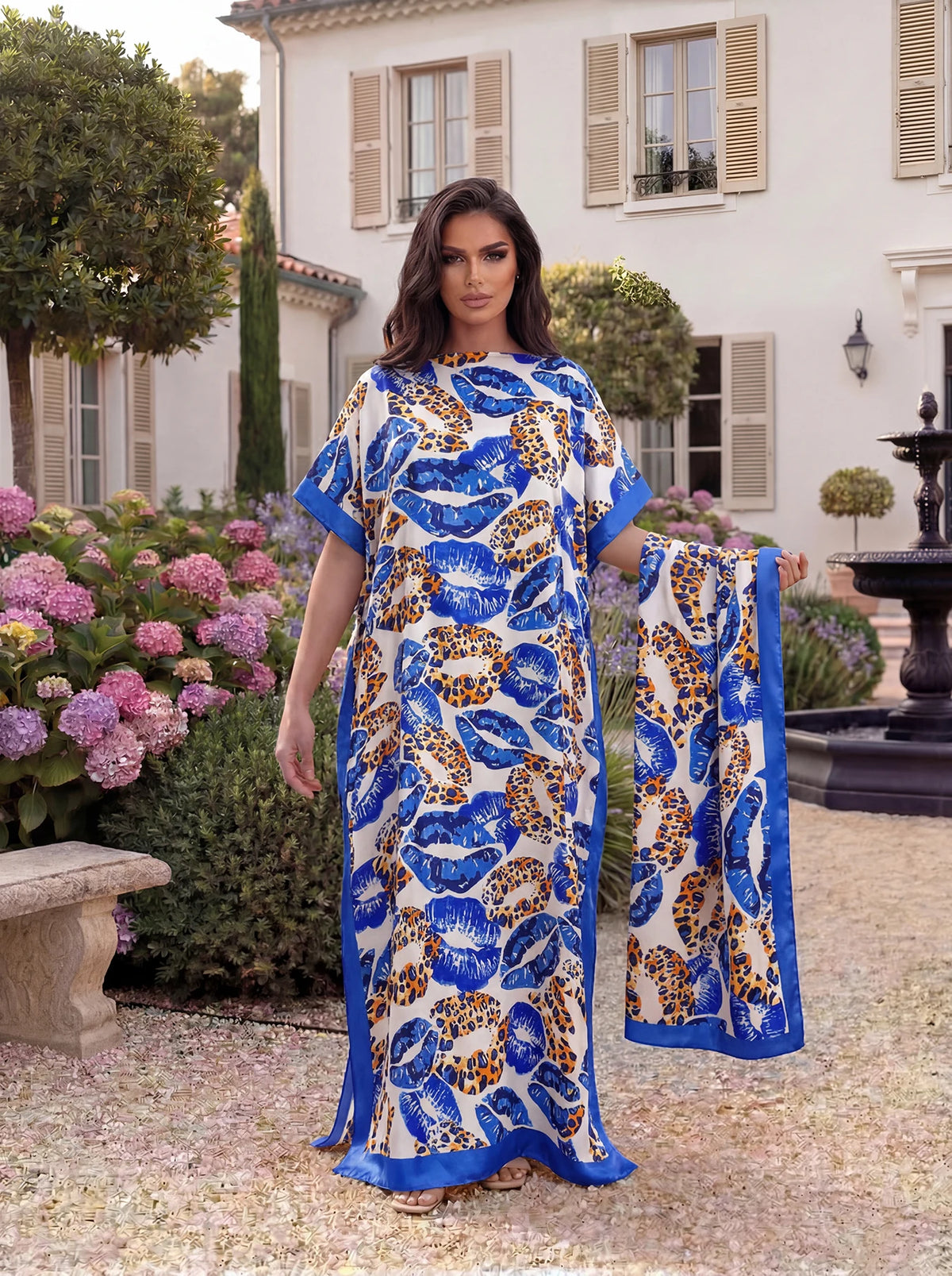 Eine Frau präsentiert ein blau-orange Leopardenmuster-Satin-Abaya-Schal-Set in einem Garten.