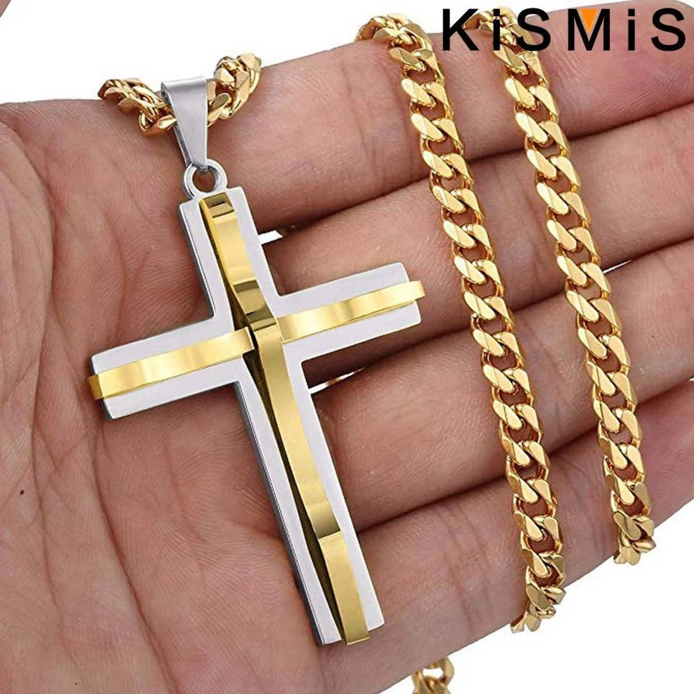Una mano sostiene un colgante de cruz de acero inoxidable con cadena de oro y detalles de plata.