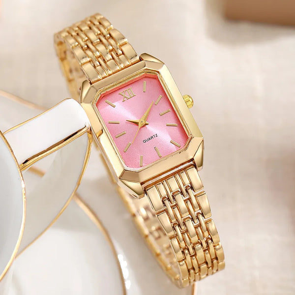 A gold minimalist quartz watch with a pink dial and rose gold accents is shown on a white plate.