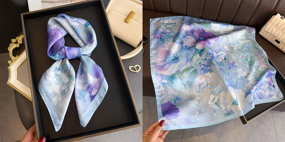 A light blue floral print silk scarf featuring purple and green flowers displayed in a black frame.