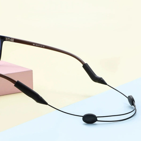 A close-up of a black universal adjustable eyewear retainer strap with a brown frame resting on a light background.