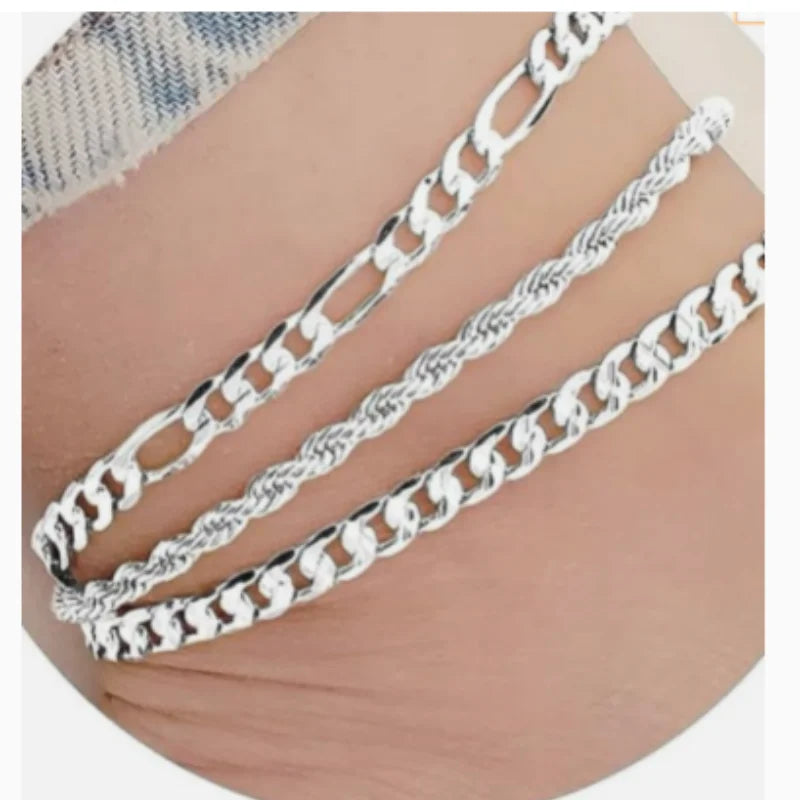 A set of three silver-colored flat snake chain anklets displayed on a person's ankle.