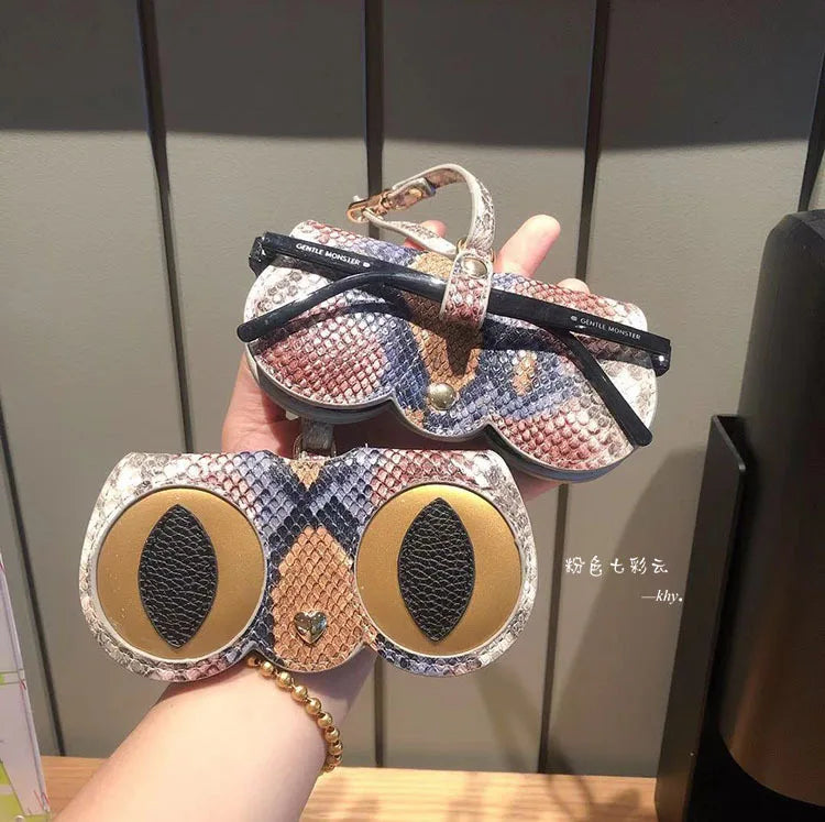 A hand holds a portable eyewear storage pouch featuring a patterned design with gold accents.