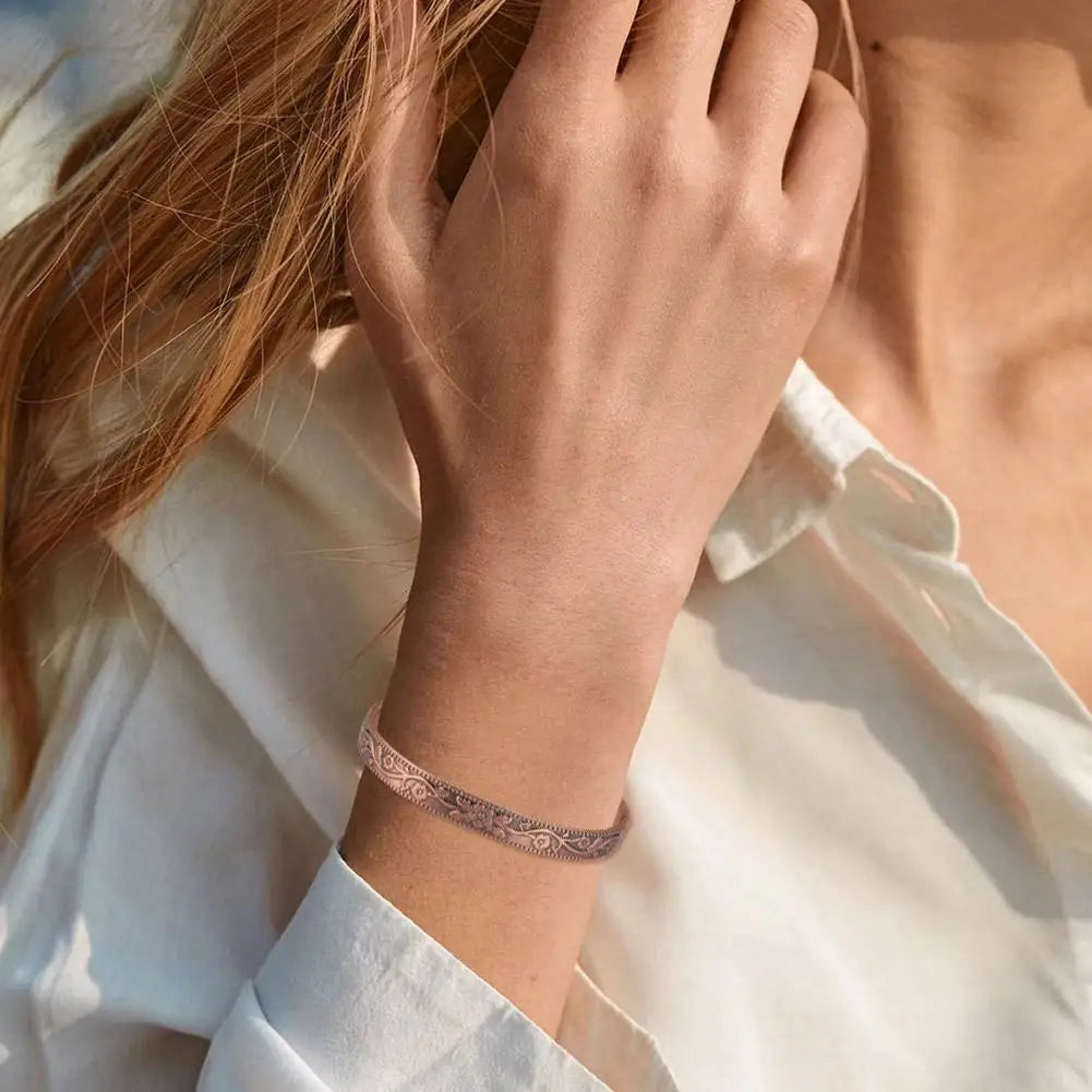 A close-up of a woman's wrist wearing a vintage flower engraved copper bracelet and ring set.