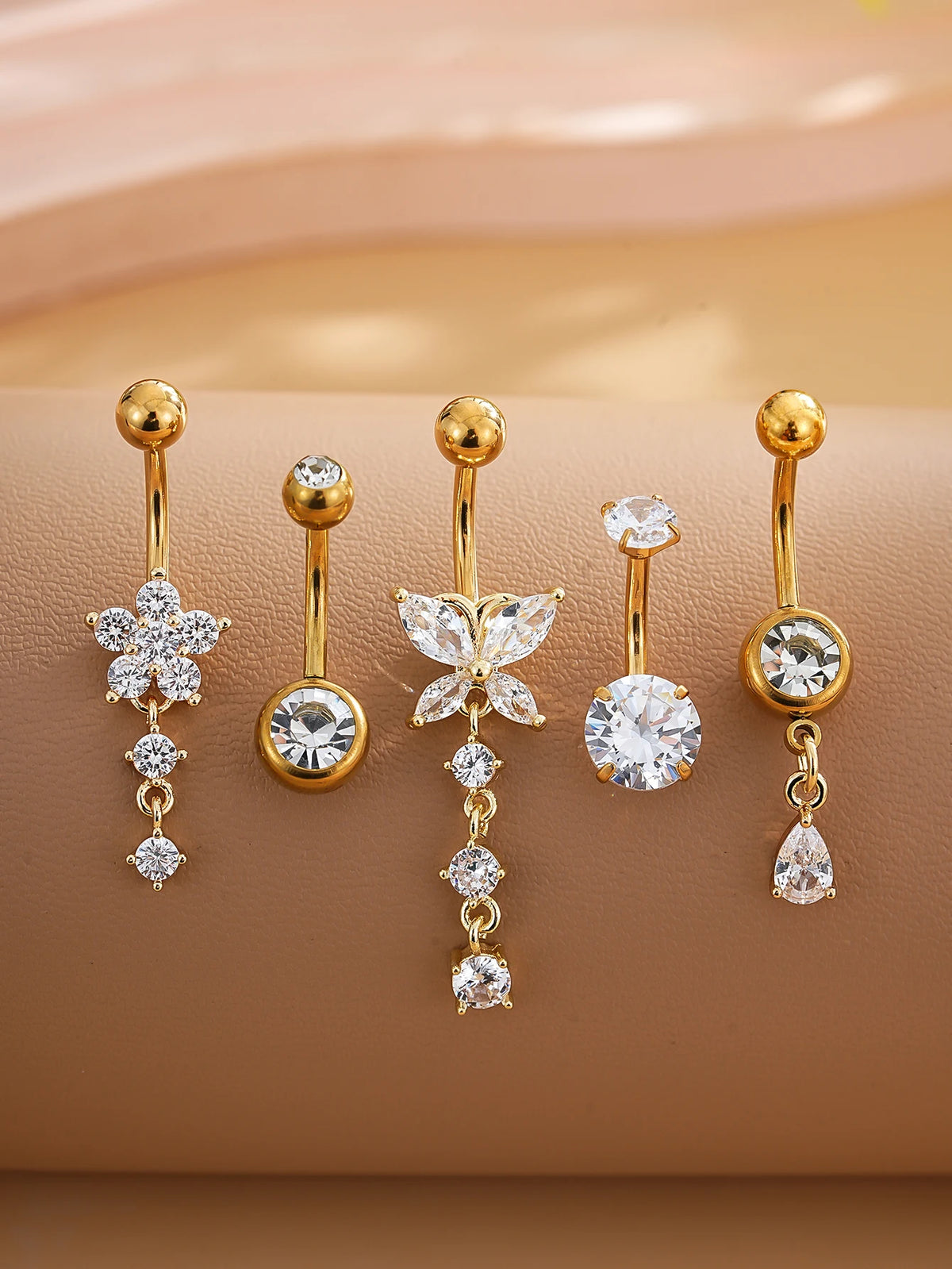 A set of five gold stainless steel dangled belly button rings featuring various diamond and gemstone designs.