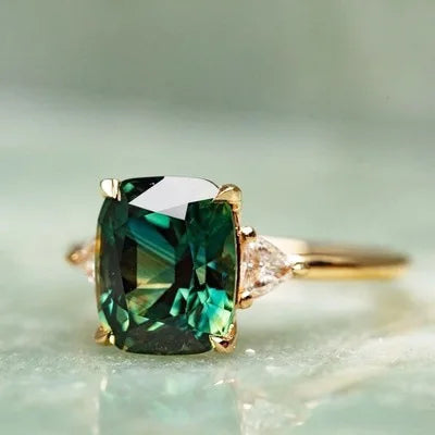 A vintage square gemstone four-claw ring featuring a deep green emerald cut stone on a gold band.