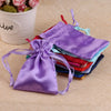 A stack of purple, blue, and red satin drawstring pouches for jewelry gifts on a beige surface.