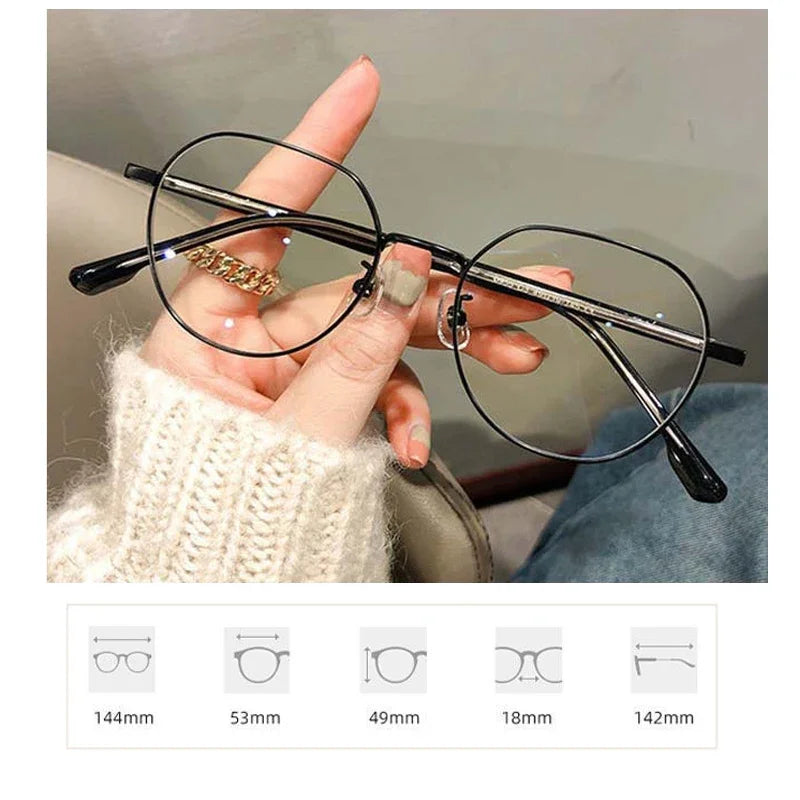 Une main tient une paire de lunettes noires à monture métallique fine sur un arrière-plan flou.