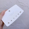 A white card displaying three gold-toned stud earrings designed by Koreas