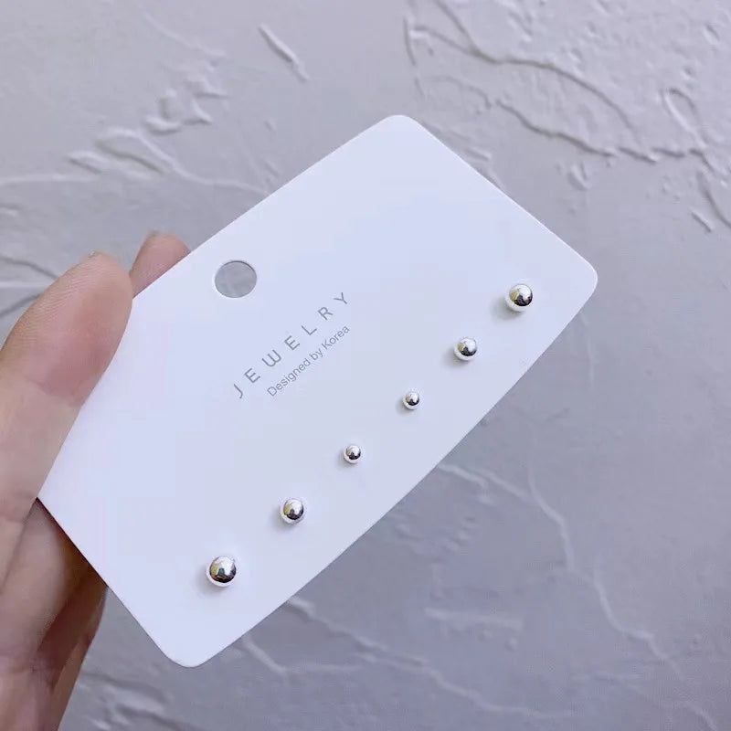 A white card displaying three gold-toned stud earrings designed by Koreas