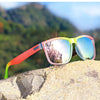 Pink and yellow gradient square polarized sunglasses resting on a rock outdoors.