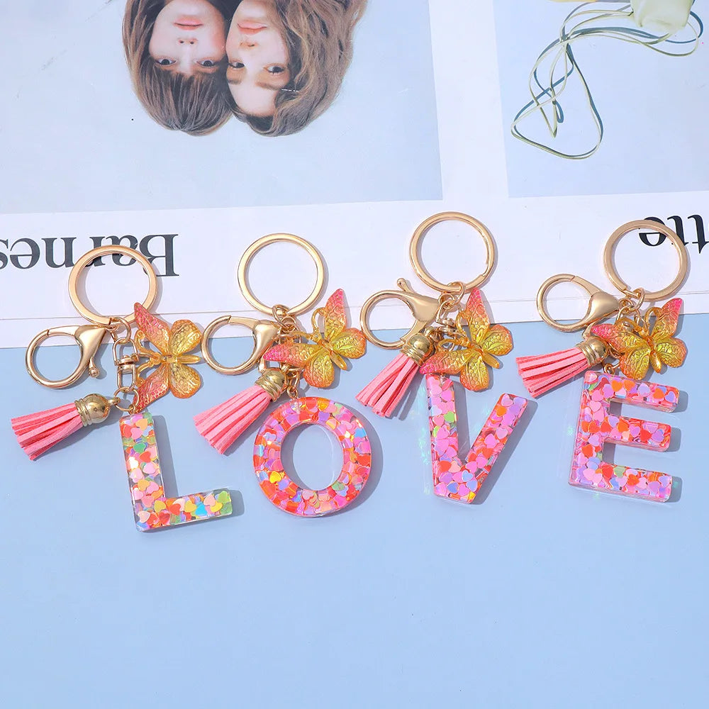 Alphabet letter acrylic keychains spelling LOVE with pink butterfly tassels