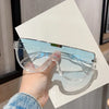 A hand holds a pair of clear vintage cat eye sunglasses with UV400 protection against a white surface.