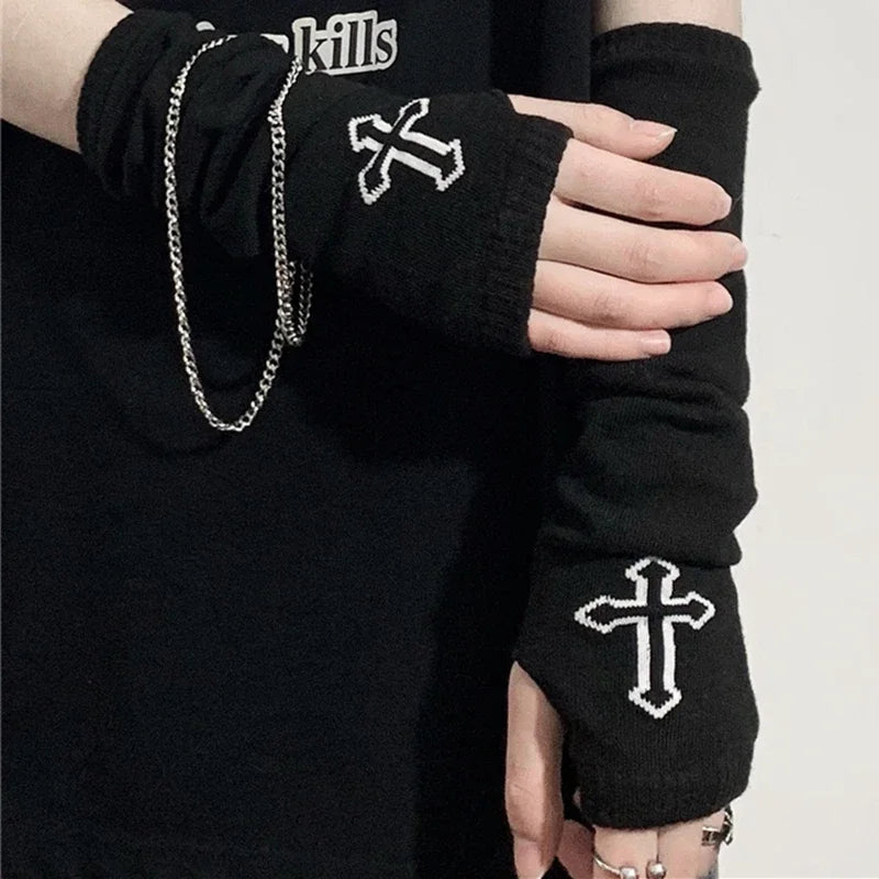 A close-up of a person wearing black knitted fingerless gloves with white embroidered crosses on the cuffs.