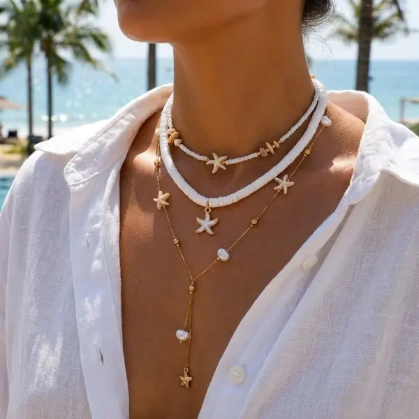 A close-up of a woman wearing a layered white beaded necklace featuring starfish and pearl charms against a bright outdoor ba