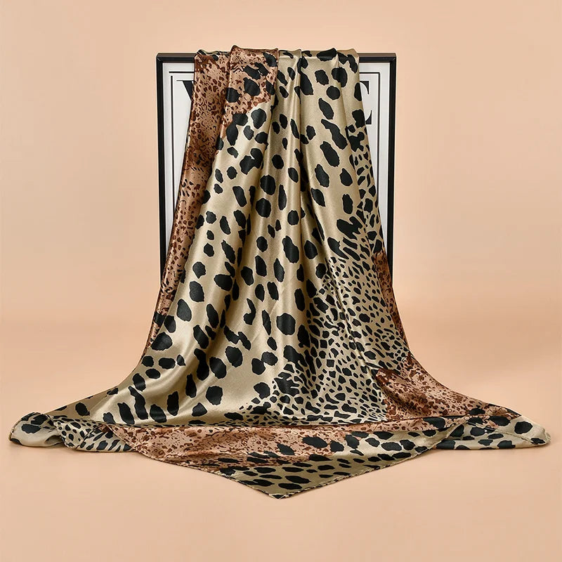A draped leopard print square satin scarf in beige and brown tones displayed against a neutral background.