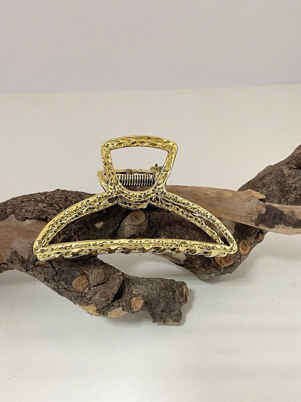 Gold metal hair claw clips with decorative beads resting on a piece of driftwood.