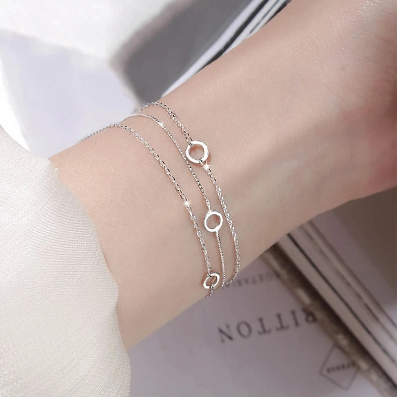A close-up of a sterling silver double heart charm bracelet worn on a wrist against a light background.