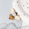 Broche ton or avec motif d'abeille, éléments blancs et noirs et une touche orange.