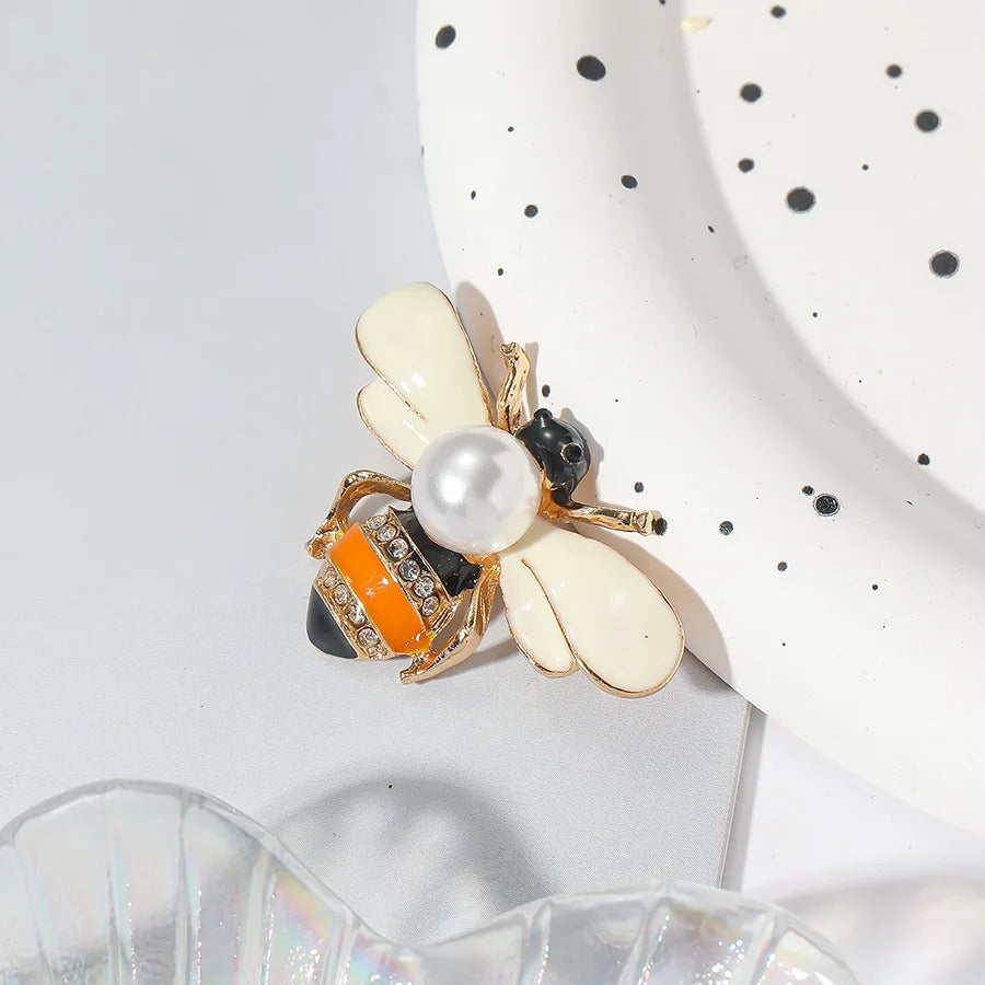 Broche ton or avec motif d'abeille, éléments blancs et noirs et une touche orange.