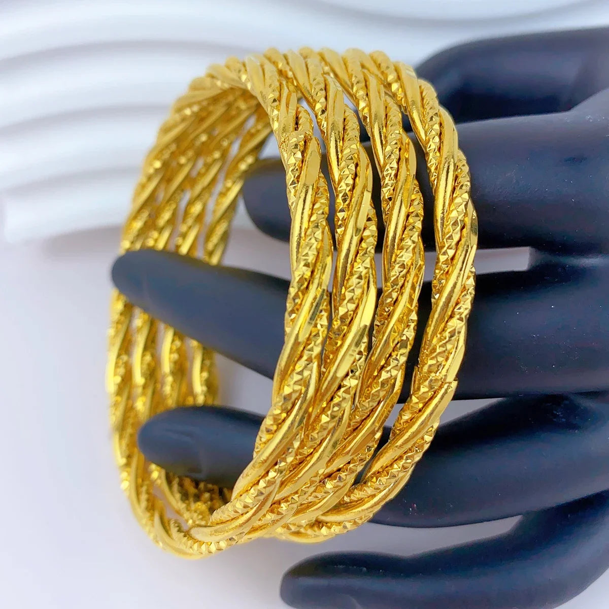 Ein Stapel dicker, geflochtener 24K-Goldfarb-Armreifen wird auf einer Hand präsentiert.