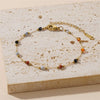 A gold-toned beaded jewelry set featuring various colored stones laid on a light beige surface.