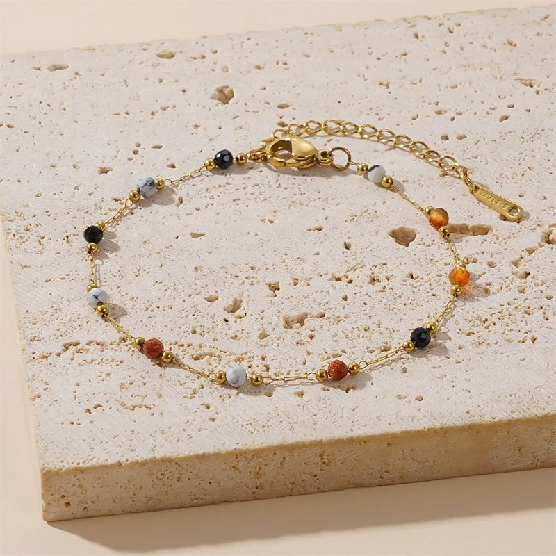 A gold-toned beaded jewelry set featuring various colored stones laid on a light beige surface.