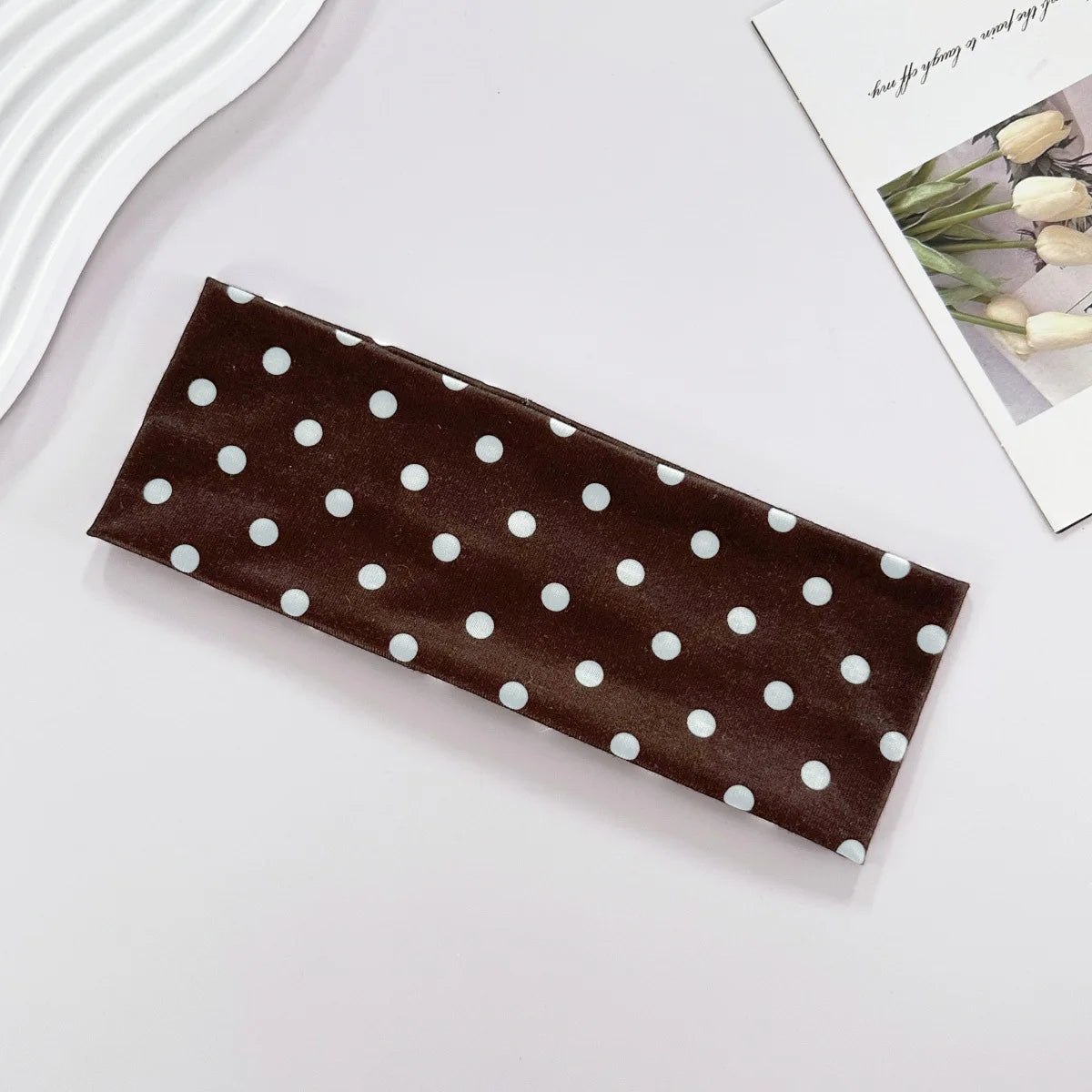 A dark brown fabric headband with white polka dots is displayed on a white surface.