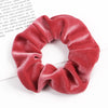 A close-up of a deep red velvet scrunchie, showing its soft texture and gathered fabric.