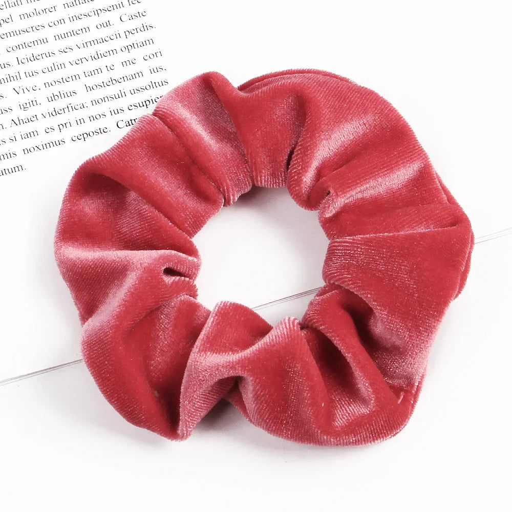A close-up of a deep red velvet scrunchie, showing its soft texture and gathered fabric.