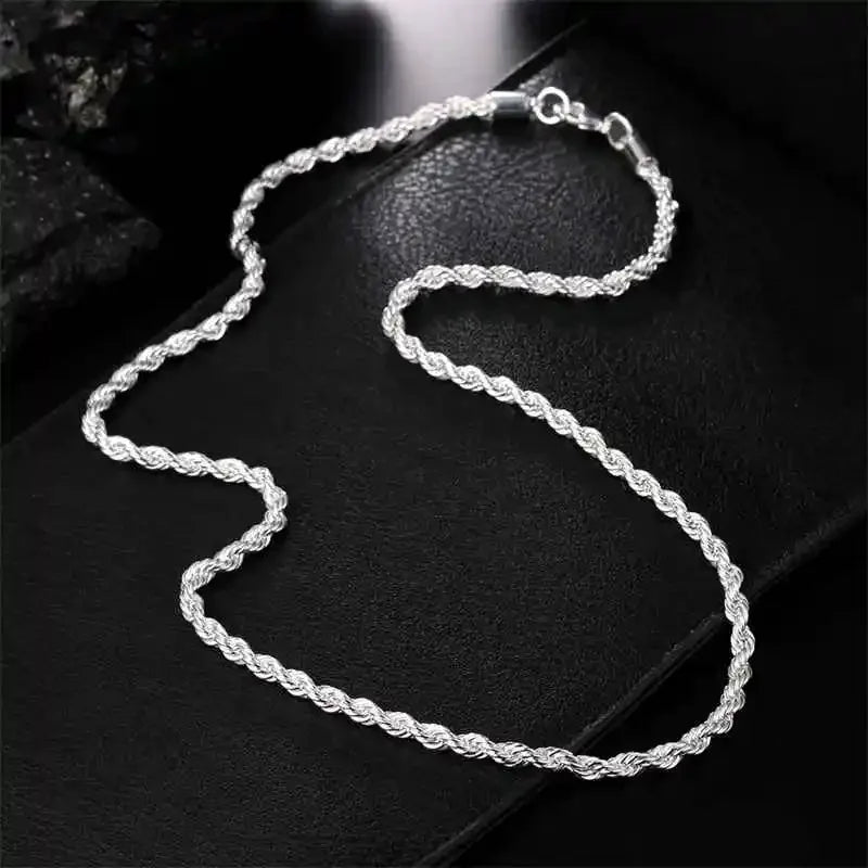 A delicate silver rope charm necklace laid on a black surface.