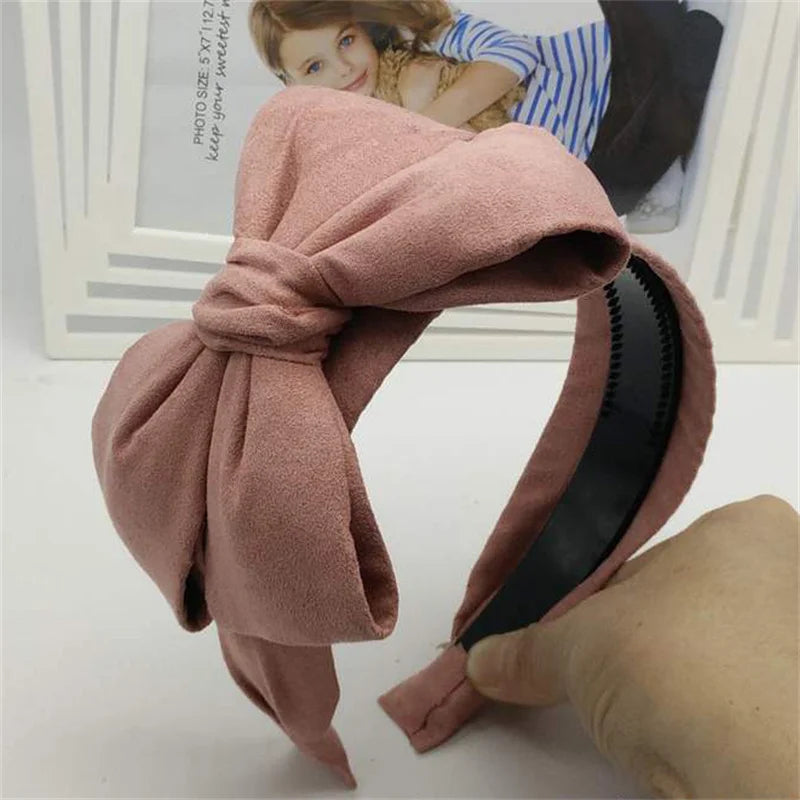 A soft dusty rose wide bow headband tied around a hand, shown next to a framed photo.