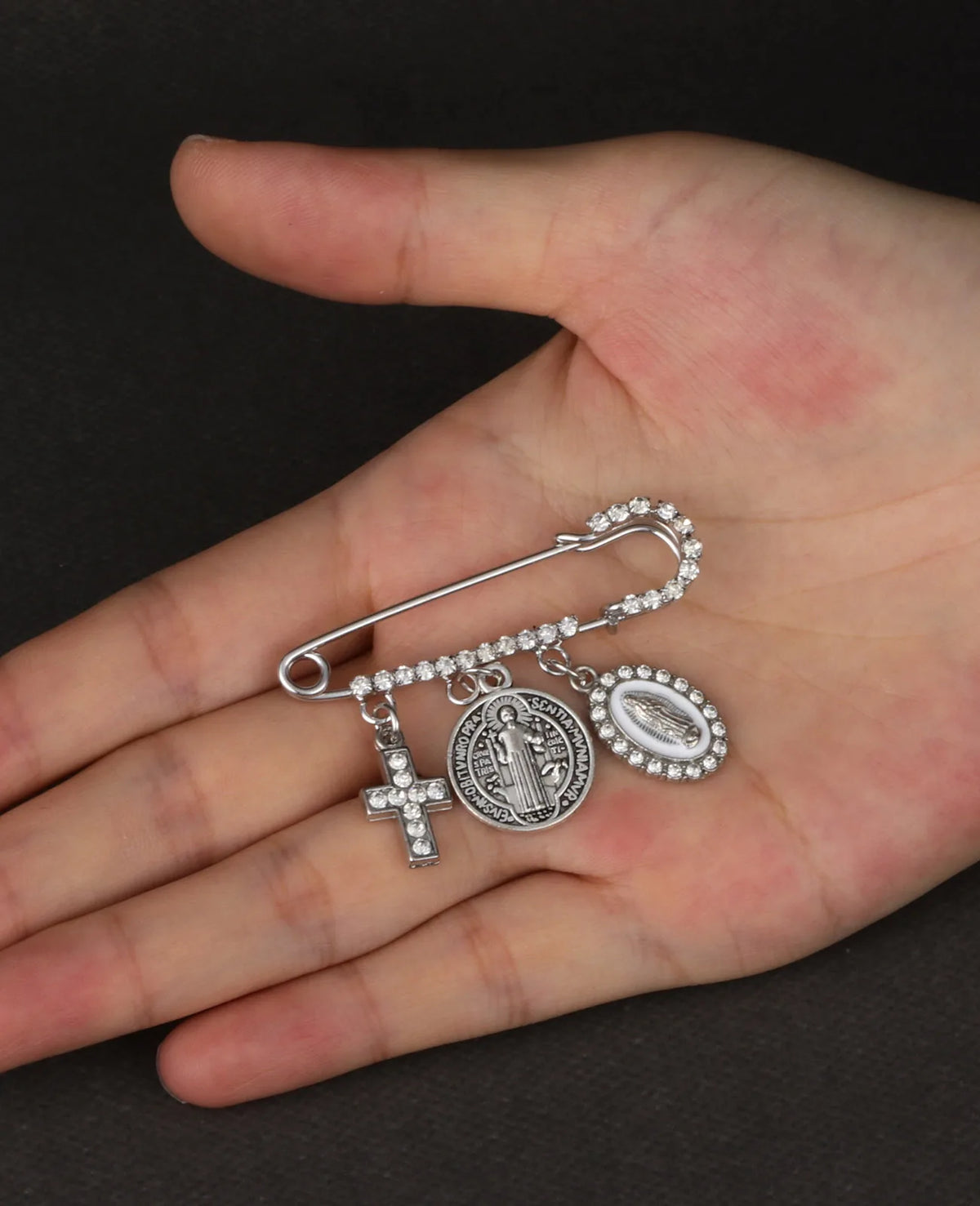 Silbernes St. Benedikt-Medal-Anstecknadel mit Kreuz und Darstellung der Jungfrau Maria in der Hand einer Person gehalten.